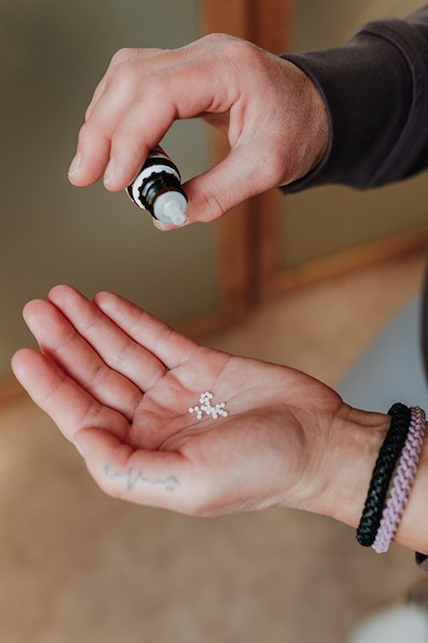 Hand mit homöopathischen Globuli aus einer Flasche