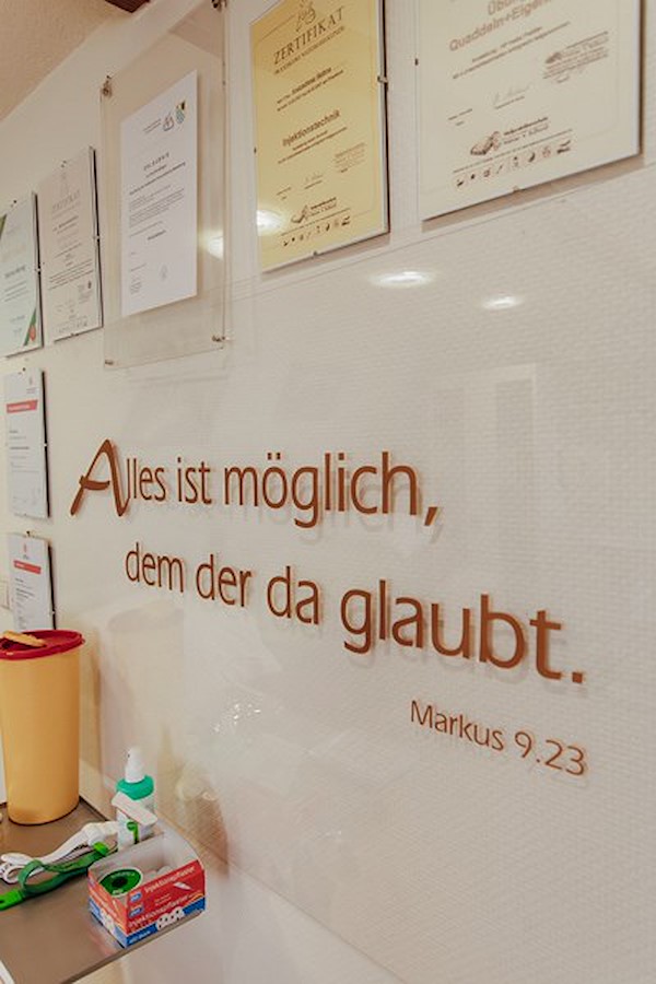 Praxiswand mit Bibelzitat und Zertifikaten